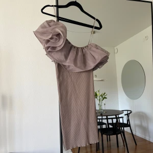 Beige one shoulder klänning med volang - Säljer en beige, tight kortklänning med en stor volangdetalj över ena axeln och smal axelrem på andra sidan. Klänningen har en ribbad struktur 🤎