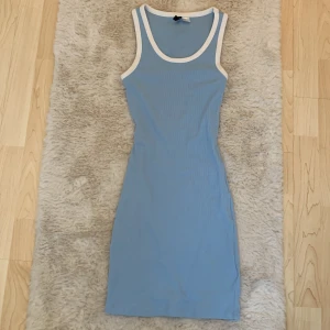 Blå ärmlös klänning från Divided - Snygg blå ärmlös klänning från Divided med vita kanter. Klänningen är ribbad och har en tight passform som framhäver figuren. Perfekt för sommaren!🌺 Nästan aldrig använd