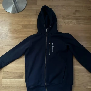 Mörkblå hoodie från Sail racing - Säljer en snygg mörkblå hoodie från Sail racing med dragkedja framtill. Perfekt för kyliga dagar med sin bekväma passform och huva. Den har en diskret logga på bröstet och ribbade muddar vid ärmslut och nederkant. Storlek S i väldigt bra skick! Skriv för funderingar!