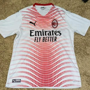 AC Milan tröja (Puma) - AC Milan bortatröja från Puma med röd och vit grafisk design framtill. V-ringning med röd krage och klubbmärke på bröstet. Stora svarta Puma-loggor och sponsortryck på framsidan. (Storleken passar S och M) pris kan även diskuteras 😄
