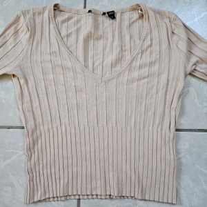 Beige ribbad tröja från Brave Soul - Säljer en stilren beige ribbad tröja från Brave Soul. Tröjan har en v-ringad design och långa ärmar, perfekt för en avslappnad look. Den är tillverkad i ett mjukt material som ger en skön passform. Använd fåtal gånger