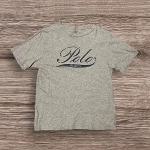 Grå t-shirt från Polo Ralph Lauren - Snygg grå t-shirt från Polo Ralph Lauren med klassisk logga tryckt framtill. T-shirten har rund hals och är tillverkad i mjuk bomull, perfekt för en avslappnad stil.