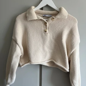 Beige stickad tröja från Zara - Säljer en beige stickad tröja från Zara med krage och knappar framtill. Tröjan är croppad och har långa ärmar. Sparsamt använd!