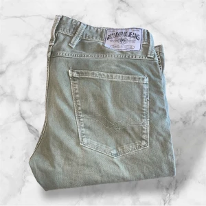 Replay Anbass gröna jeans - Snygga gröna Replay Anbass jeans med klassisk femficksdesign och dragkedjegylf. Byxorna har raka ben och diskreta sömdetaljer på bakfickorna. Perfekta för dig som gillar stilrena jeans med modern passform. Har ett silver R i metal på bakfickan! W31 L34