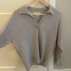 Grå kashmirtröja från Soft Goat - Supermjuk grå kashmirtröja från Soft Goat med klassisk krage och v-ringning. Tröjan har lång ärm och ribbade muddar vid ärmslut och nederkant. Perfekt för dig som gillar en clean och stilren look. Sparsamt använd i storlek S.
