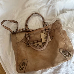 Beige balenciaga liknade väska💘💞 - Stor beige axelväska i med coola detaljer som dragkedja framtill, dubbla handtag och justerbar axelrem. Väskan har metallspännen och en avslappnad, lite vintage look. Perfekt för dig som vill ha plats för allt och gillar en unik stil💘prislappen på!