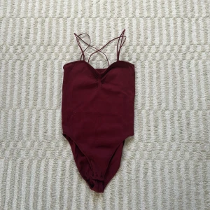 Vinröd ribbad body från ONLY - Supersnygg vinröd body från ONLY med tunna korsade axelband och ribbad struktur. Den har en lätt v-ringning och knäppning i grenen för enkel på- och avtagning. Storlek S/M, endast använd 1 gång