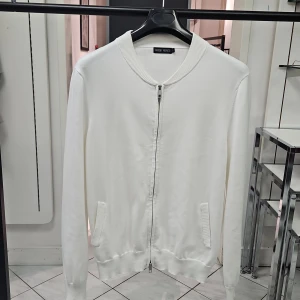 Vit cardigan  från Antony Morato - Snygg vit cardigan från Antony Morato med dragkedja framtill och ribbade muddar. Cardigan har en clean look med två fickor och diskret metallogo bak i nacken. Perfekt för dig som gillar stilren och enkel design. Material: Bomull. Dubbelsidig dragkedja 