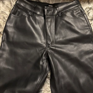 Svarta skinnbyxor från BikBok - Snygga svarta byxor i skinnimitation från BikBok. Klassisk femficksmodell med bälteshällor och raka ben. Perfekt för alla tjejkvällar! Haft på mig dessa 2 gånger ungefär.