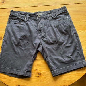 Mörkblå shorts från CTRL CO - Snygga mörkblå shorts från CTRL CO med klassisk femficksdesign och knappgylf. Tillverkade i mjuk bomull för en skön känsla. Perfekta för varma dagar och har en stilren look som passar till det mesta. Midja med hällor för bälte och raka ben. Midjemåttet är 99