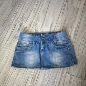 Blå jeanskjol från Monday - Snygg blå jeanskjol från MonDay med klassisk femficksdesign, dubbla knappar fram och broderad logga på bakfickan. Kjolen är kort och har bälteshällor, perfekt till sneakers eller boots. Färgen är ljusblå denim med lätt slitning för en cool vibe.