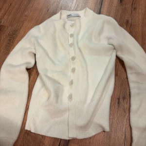 Vit kofta från Zara med pärlknappar - Superfin vit kofta från Zara med långa ärmar och dekorativa pärlknappar framtill. Mjuk och mysig känsla, perfekt för lager på lager. Ribbstickade muddar vid ärmslut och nederkant ger en snygg passform.