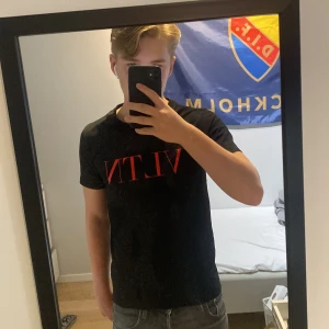 Svart VLTN t-shirt från Valentino - Säljer en svart t-shirt från Valentino med röd VLTN-logga på bröstet. Klassisk passform och rund halsringning. Perfekt för dig som gillar stilrena och trendiga plagg med exklusiv känsla. Sitter rätt tajt på mig som är 175