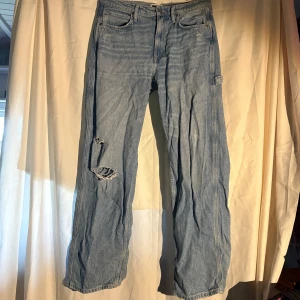 Ljusblå Lee jeans med slitning - Ljusblå jeans från Lee H&M. Jeansen har en snygg sliten detalj med hål på ena knät och Lee-logga på bakfickan. Tillverkade i bomull och har en avslappnad, rak passform.