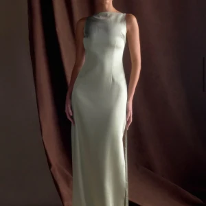 Ljusgrön långklänning i satin från Meshki - En ljusgrön långklänning från Meshki (namn: Violet) i satin. Materialet är tjockt, vilket är suveränt då vissa tunna satinklänningar oftast kan kännas bräckliga, och klänningen är form-fitted. Klänningen har ärmlös design, rak siluett och hög halsringning. Den är i XL men kan enkelt passa M/L - vilket var anledningen till varför den inte kunde behållas. Packas i originalpaketet!