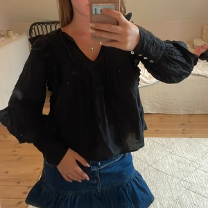 Svart blus med knyt från BikBok XS - Svart blus från BikBok i storlek XS med v-ringning och knyt framtill. Långa puffiga ärmar med knappar vid ärmslut och fina veckdetaljer framtill. 