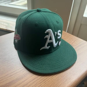 New Era Keps - Snygg grön 59FIFTY keps från New Era med Oakland A's logga broderad framtill och World Series 1989 patch på sidan. Kepsen har platt skärm, broderade detaljer. Kepsen är i nyskick och är i st 7 1/4( 57.7cm), hör av er vid mer frågor 