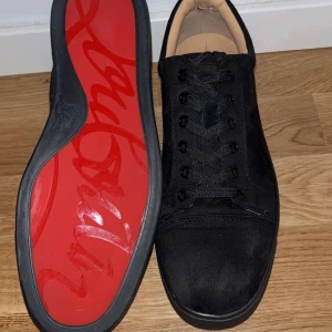 Christian Louboutin Skor - Knappt använda och Snygga svarta sneakers från Christian Louboutin med ikonisk röd sula. Skorna har en stilren design i mocka och klassisk snörning. Perfekta för dig som vill sticka ut med exklusiva detaljer och lyxig känsla. Kommer med Christian Louboutin dustbag! Pris går att förhandla