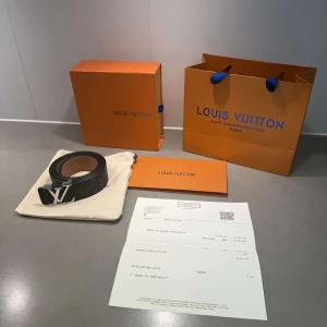 Louis Vuitton svart monogram skärp - Säljer ett svart Louis Vuitton skärp i skinn med klassiskt monogrammönster och en stor silverfärgad LV-logga som spänne. Bältet har en lyxig känsla och insidan är ljusbrun. Perfekt accessoar för att lyfta din outfit.