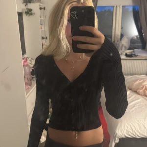 Svart ribbad kofta med v-ringning - Säljer en svart ribbad kofta med v-ringning och knappar framtill. Modellen är croppad och har långa ärmar. Säljs då den aldrig används💘