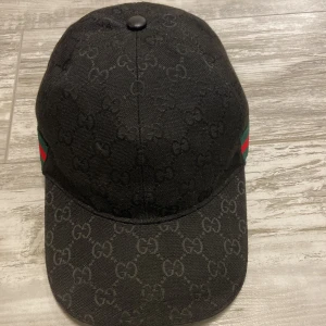 Svart gucci keps - Snygg svart keps från Gucci med klassiskt GG-monogram över hela kepsen. Kepsen har justerbart spänne bak i skinn och ikoniska gröna och röda ränder på sidorna. ||Pris går att diskuteras||