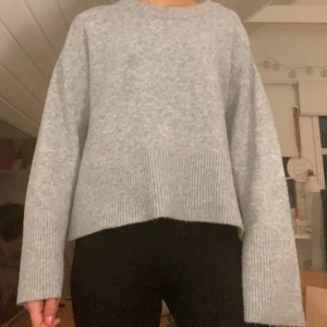 Ljusgrå stickad tröja med vida ärmar - Supermjuk ljusgrå stickad tröja med bred ribbad kant nertill och på ärmsluten. Tröjan har en loose passform och långa, vida ärmar som ger en chill vibe. Perfekt för lager-på-lager och passar till allt från jeans till kjol.