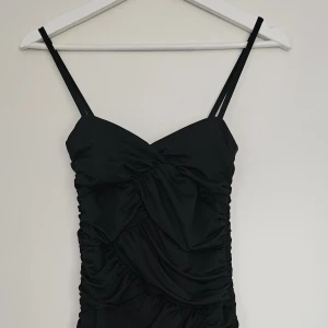 Svart draperad festklänning från H&M  - Snygg svart stretchig klänning i svart med draperad/ruchad design. Figurnära modell med smala axelband. Dragkedja bak Storlek: XS Fint skick - endast använd ett par gånger..