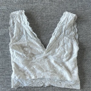 Vit spetsig linnetopp från Amisu XS - Supersöt vit linnetopp från Amisu i storlek XS. Toppen är helt täckt av blommig spets med v-ringning och breda axelband. Perfekt för lager på lager eller som statement-piece. Snygg och feminin look med fina spetsdetaljer.