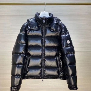 Svart Moncler pufferjacka med glans - Snygg svart pufferjacka från Moncler med glansig finish och klassisk logga på ärmen. Jackan har hög krage, dragkedja framtill och två fickor med dragkedja. Perfekt för kalla dagar när du vill hålla stilen och värmen.