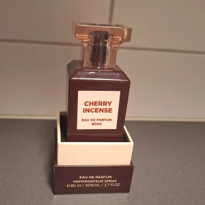 Cherry Incense Eau de Parfum 80ml - Cherry Incense från Fragrance World är en eau de parfum på 80 ml med en djup rödbrun glasflaska och transparent lock. Doften har rökiga, vedartade och läderaktiga toner med varm kryddighet. Passar både kvinnor och män som gillar unika och intensiva dofter.(Några ml taget)