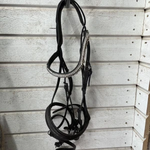 Svart träns med glittrigt pannband - Säljer ett svart träns i skinn med ett snyggt glittrigt pannband i silver. Tränset har mjuk vaddering och flera justerbara remmar. Perfekt för dig som vill sticka ut lite extra i stallet.