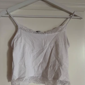 Vit spetskantad linnetopp FB Sister XS - Supersöt vit linnetopp från New yorker i storlek XS. Tunt axelbandslinne med fina spetsdetaljer längs både halsringning och nederkant. Perfekt att styla med jeans eller kjol för en fräsch look. Mjuk och skön bomullskänsla.