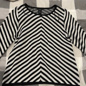 Randig svartvit stickad tröja Lindex - Snygg stickad tröja från Lindex i storlek S. Tröjan har ett coolt svartvitt randigt mönster med V-formade linjer framtill och långa ärmar. Perfekt för dig som gillar grafiska mönster och vill sticka ut lite extra.