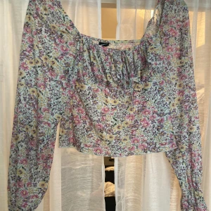 Blommig blus från Gina Tricot - Supersöt blommig blus från Gina Tricot i storlek S. Toppen har långa ärmar och volangdetalj vid halsringningen. Färgerna går i lila, rosa, gul och grön på en ljus botten. Perfekt för vår och sommar när du vill ha en romantisk vibe.