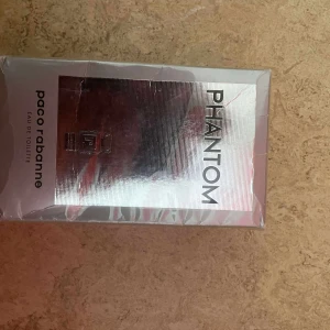 Paco Rabanne Phantom EdT - Phantom Eau de Toilette från Paco Rabanne i en futuristisk silverfärgad kartong. Doften är modern och maskulin, och förpackningen har en spegelblank finish med tydlig logga och text. Perfekt för dig som gillar unika och trendiga parfymer.