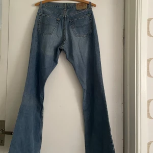 Bootcut jeans från John Pearson & Son - Bootcut jeans i klassisk ljusblå denim från John Pearson & Son, modell 652 Bootcut. Storlek W 33 och L 32. Jeansen har fem fickor, raka ben med lätt utsvängning nertill och snygga kontrastsömmar. Perfekta för dig som gillar retrovibbar och avslappnad stil. (Midjemått 85 cm. Innerbenlängd 84 cm. Total längd 108 cm. Lårvidd 53 cm. Knävidd 42 cm. Fotvidd 53,5 cm)