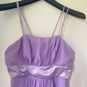 Ljuslila kortklänning med satinband - Superfin ljuslila klänning med dubbla smala axelband och ett glansigt satinband under bysten. Klänningen är ärmlös, har lätt vidd i kjolen och stängs med dragkedja bak. Perfekt för dig som vill sticka ut med en söt och feminin look.