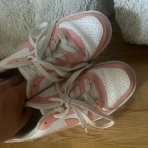 Nike sneakers  - Nike Dunk Low sneakers i vitt och ljusrosa med perforerad tå och klassisk swoosh. Skorna har snörning och platt sula, tillverkade i syntet och skinn. Perfekt för dig som vill ha en clean och trendig look.