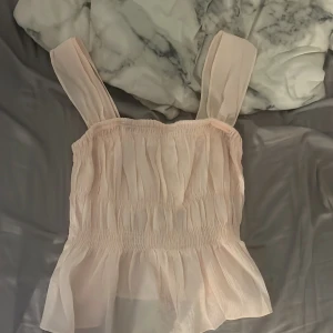 Volang topp  - Supersöt ljusrosa linnetopp från H&M med breda axelband och volangig nederdel. Toppen har smockad midja och är gjord i ett tunt, flowy material. den är ny kostar 249kr i butik