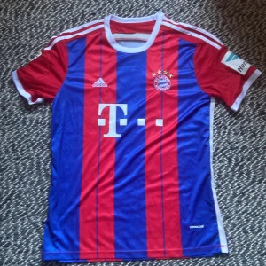 Bayern München Lewandowski  - HELT NY!Säljer en officiell Bayern München fotbollströja med Lewandowski #9 på ryggen. Tröjan är röd och blå med vita detaljer, Adidas-logga och klubbmärke på bröstet. Tillverkad i lätt och ventilerande polyester med klassiska ränder och korta ärmar.
