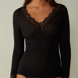 svart intimissimi  - supersnygg svart långärmad topp med v-ringning och spetsdetaljer runt halsen och ärmsluten. Tight passform som framhäver figuren och ger en elegant vibe. Perfekt att styla med jeans eller kjol för en trendig look.