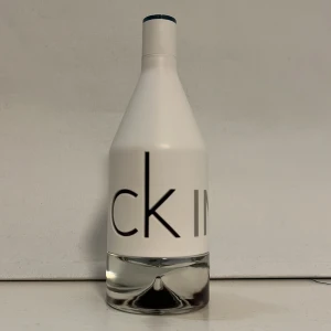 Calvin Klein IN2U Him parfym - Fräsch parfym från Calvin Klein, IN2U Him. Flaskan är vit med minimalistisk design och tydlig text i grått och svart. Nedre delen är genomskinlig och visar den klara vätskan. Perfekt för dig som gillar stilren och modern look.