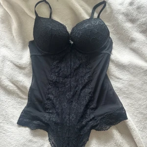 Svart spetskorsett med bygel - Svart korsett från H&M med vadderade kupor och bygel, täckt av blommig spets framtill och mesh på sidorna. Justerbara axelband och fina spetsdetaljer längs nederkanten ❣️storleken är ca 70/75B, 70/75C