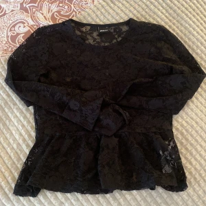 Svart spetsblus från Gina Tricot - Supersöt svart blus i spets från Gina Tricot med lång ärm och volang nertill. 