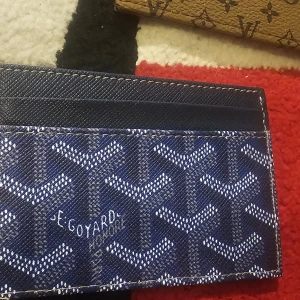 Blå Goy plånbok med mönster - Säljer en blå plånbok från GJ d med deras ikoniska grafiska mönster i vitt och grått. Plånboken har flera kortfack och är tillverkad i ett tåligt syntetmaterial med präglad yta. Perfekt för dig som vill ha något stilrent och unikt i fickan.