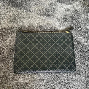 Svart kuvertväska By Malene Birger - Stilren svart kuvertväska från By Malene Birger med grått rutmönster och guldfärgad dragkedja. Går att använde som clutch men även som vanlig väska då väskhandtaget är avtagbart. Finns några enstaka repor på väskan som ni ser på bilderna