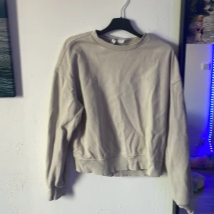 Beige sweatshirt från H&M Divided XS - Enkel och stilren beige sweatshirt från H&M Divided i storlek XS. Tröjan har rund halsringning, långa ärmar och ribbade muddar vid ärmslut och nederkant. Perfekt för en chill och avslappnad look.