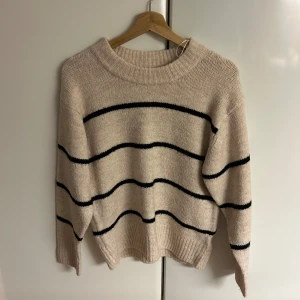 Beige randig stickad tröja Gina Tricot - Beige stickad tröja från Gina Tricot med svarta horisontella ränder. Tröjan har en rund halsringning, ribbade muddar och lång ärm. Perfekt för dig som gillar en enkel men snygg stil med lite oversized känsla. Inte fri frakt! 