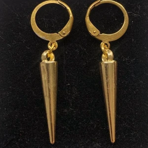 Guldiga örhängen med spetsig hängande detalj - Snygga örhängen i guld med rund ring och en lång, spetsig hängande detalj. De har en modern och edgy vibe, perfekta för att lyfta din stil. Passar dig som gillar statement-smycken och vill sticka ut.