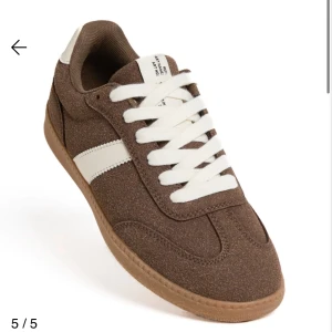 Bruna sneakers med vit detalj - Snygga bruna sneakers i mocka med vit sula och vita snören. Skon har en vit rand på sidan och en klassisk rund tå. Perfekt för dig som gillar retrostil och vill ha något som sticker ut lite extra. Prislappen finns tyvärr inte men skorna är helt nya har bara testat dom! För småa. Ordinarie pris : 300kr